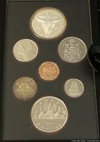 Front view of the 7 coins in original black presentation case showing the reverse sides with detailed designs including animal motifs and Canadian symbols.