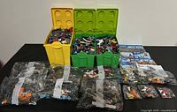 Overview of three large plastic containers filled with assorted LEGO bricks and sealed plastic bags of LEGO components with instruction manuals visible on the right.