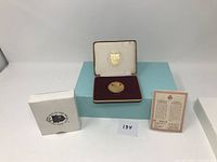 Photo showing coin in presentation box with certificate and white outer box.