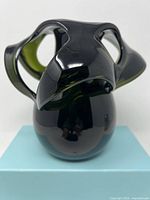 Front view of dark green glass handmade vase with abstract folded top design.
