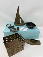 Photo showing all five items: brass sailboat, two small ashtrays, brass basket, and metal bottle opener on a blue box.
