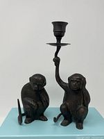 Two bronze monkey figurines displayed on a light blue platform, one holding a candle holder.