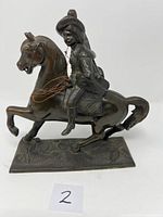 Front side view of cast metal spelter sculpture showing Spanish man in wide-brimmed hat riding horse with front leg raised, wire attached to rider's hand.