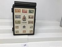 Front view of the black plastic hinged case showing thirteen Canadian Centennial Issue stamps arranged in a grid on a white card with central emblem and text.
