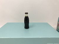 Miniature Coca-Cola bottle lighter upright on blue surface.