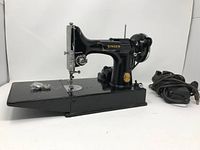 Singer Featherweight 221 sewing machine with power cord and bobbin accessories on fold-flat base
