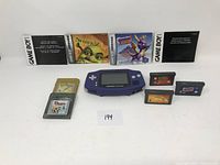 Full lot image showing purple Game Boy Advance console, seven game cartridges, and three instruction manuals.