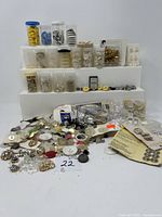 Full assortment of vintage buttons and fasteners arranged on display with various plastic containers and loose items in front.