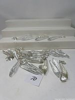 Top view of 24 clear chandelier crystals laid out on a white surface with metal rings attached for hanging. The crystals have a faceted elongated teardrop shape.