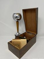 Wooden box file holder with open lid and vintage postcards inside, next to metal trophy with wooden stand.