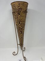 Front view of the cone shaped metal vase on stand with embossed leaf and berry design.
