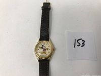 Front view of the Lorus Mickey Mouse wristwatch showing the gold-tone case, white dial, Mickey Mouse figure, and worn brown leather strap.