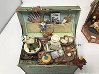Photo showing the open music box with multiple small toys inside including a marionette puppet, spinning top, doll in bonnet, castle block, and others.