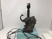 Front and side view of peacock-shaped table lamp showing detailed feather sculpting and lamp socket on top.