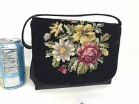 Front view of black vintage clutch purse showing detailed cross stitched floral embroidery on flap with pink rose, yellow flowers, and white daisy.