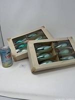 Two opened vintage cardboard boxes containing 12 light blue elongated glass Christmas bulbs with reflective finish, showing packaging condition.