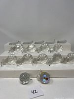 Front view of 9 larger clear leaf-shaped chandelier crystals with metal hooks and 2 globe-shaped crystals, one clear faceted and one iridescent with reflective sheen.