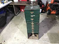 Front view of green metal watchmaker’s cabinet showing seven drawers and top-mounted winder