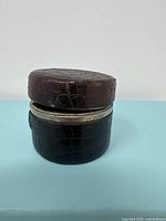 Closed view of round, leather wrapped travel inkwell with quilted pattern on the exterior.
