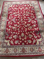 Full view of the traditional red area rug with a floral design and bordered edges.
