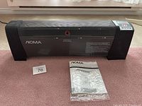 Full view of black NOMA digital baseboard heater placed on carpet, with instruction manual and lot number card in front.