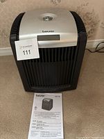 Black and silver Beurer LW 110 air washer device on carpet with instruction manual in front showing product image and multi-language instructions.