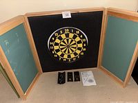 Full view of Double Top dart board with wooden triptych-style frame with chalkboards on inner panels, three dart sets below the board, and instruction sheet.