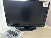 Front view of 26 inch FLUID LCD TV/DVD combo on stand with remote and manual