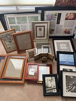 Grouped display of assortment of frames on carpet, various sizes and finishes including teak wood frames, collapsed photo collage frames, and small metal frames.