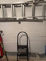 Photo showing black 2-step ladder standing upright against a white brick wall