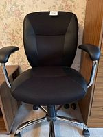 Front view of black office chair showing fabric center and leather-like sides with chrome armrests