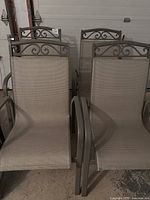 Four outdoor metal frame patio chairs with beige mesh seating and decorative scrollwork backs.