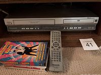 Front view of Panasonic DVD/VHS combo player with several buttons and logos visible, showing silver unit with DVD and VHS functions.