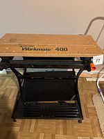 Front view of the workbench showing the wooden top with 'Workmate 400' label and foldable black metal frame with lower shelf.