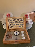 Photo of wooden box containing framed photo collage, golf balls, hockey puck, small pouch, with white Golf Marshal helmets in background