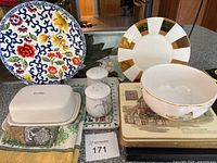 Display of tableware items including Pier 1 Imports Ralph Lauren plate, Mary Carol butter dish, salt and pepper shakers, plastic trays, and placemats.