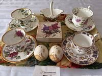 Full lot showing four bone china teacups and saucers in various floral patterns, a pair of bunny salt and pepper shakers, and floral coasters.
