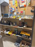 Wide view of shelves with assorted tools, hardware, wall anchors, measuring tape, screws, nails, containers, and hardware accessories