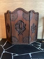 Front view of the 3-panel wooden carved fireplace screen showing detailed central and corner carvings on each panel.