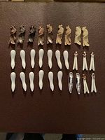 Top-down photo showing all 19 chopstick rests arranged in rows on a brown textured surface: 9 soapstone rests with carved abstract/bird shapes and 10 porcelain rests, mostly white with a few decorated pieces.