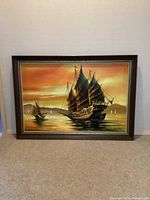 Frontal view of the framed oil painting depicting Chinese junk sailing ships in sunset lighting.