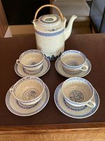 Porcelain teapot with bamboo handle and 4 matching teacups with saucers, showing tops and side angles with blue rice grain pattern