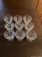 View of nine vintage clear glass dessert cups arranged in rows on a brown surface.