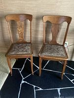 Pair of oak straight back chairs with cloth seats against a beige wall and black patterned rug.