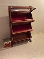 Front and side view of vintage wooden biscuit display cabinet with glass-front compartments open showing red velvet lining inside.