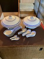 Top view of the set showing 2 ceramic serving bowls with lids and multiple ceramic spoons in blue and white pattern arranged around them.
