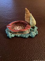 Top angled view of porcelain ashtray showing longevity character inside base, decorative floral pattern and two ornamental shapes on aqua textured base.
