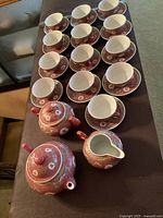 Top-down view of vintage Chinese red famille rose porcelain tea set including 13 cups and saucers arranged in rows, one teapot, one creamer, and one sugar bowl placed at the front on a table.