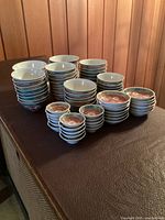Multiple stacks of bowls and sauce dishes arranged on dark surface against wood panel background