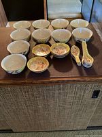 Twelve rice bowls, seven dishes and ten spoons arranged on table